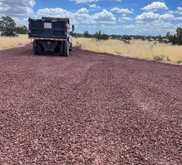 A truck on a gravel road surrounded by dry grass under a partly cloudy sky.