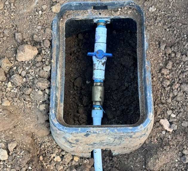 A blue water valve inside a rectangular underground casing surrounded by dirt and gravel.